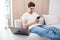 Young handsome man sitting relaxed on sofa with laptop checking his smartphone messages