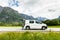 Young handsome man sitting in the trunk of his hired car and talking on the mobile phone on mountains background. Car hire. Car