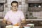 Young handsome man squints from fresh cut onion during cooking process at wooden home kitchen in classical style. Vegetables and r