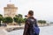 Young handsome man in sunglasses, tourist, with backpack taking pictures on a smartphone a White Tower in the center Thessaloniki