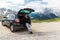 Young handsome man talking on the phone while sitting in trunk of his car and enjoy mountains view