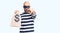 Young handsome man wearing burglar mask holding money bag with dollar symbol pointing with finger to the camera and to you,