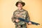 Young handsome man wearing camouflage army uniform holding shotgun smiling and laughing hard out loud because funny crazy joke