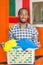 Young handsome man wearing casual clothes holding laundry basket and smiling to camera, orange wall with flags in