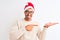 Young handsome man wearing christmas hat and glasses over isolated background amazed and smiling to the camera while presenting