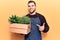 Young handsome man wearing gardener apron holding pant pot smiling happy pointing with hand and finger