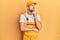 Young handsome man wearing handyman uniform over yellow background with hand on chin thinking about question, pensive expression
