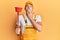 Young handsome man wearing plumber uniform holding toilet plunger covering mouth with hand, shocked and afraid for mistake