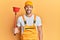 Young handsome man wearing plumber uniform holding toilet plunger looking positive and happy standing and smiling with a confident