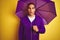 Young handsome man wearing purple umbrella over yellow isolated background scared in shock with a surprise face, afraid and