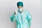 Young handsome man wearing surgeon uniform and medical mask angry and mad raising fist frustrated and furious while shouting with