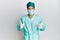 Young handsome man wearing surgeon uniform and medical mask success sign doing positive gesture with hand, thumbs up smiling and