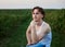 Young handsome man, wearing torn jeans and white t-shirt, sitting on yellow stool on green field, thinking. Artistic education