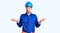 Young handsome man wearing worker uniform and hardhat doing bunny ears gesture with hands palms looking cynical and skeptical