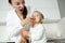 Young handsome mother feeding with peach her little son in kitchen. Mom making funny expression to make laugh her child.