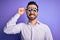 Young handsome optical man with beard wearing optometry glasses over purple background with a happy face standing and smiling with