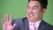 Young handsome overweight Asian businessman against green background