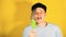 Young handsome satisfied man with dreadlocks in black cap eating ice cream on yellow background. Joyful guy in blue t