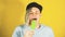 Young handsome satisfied man with dreadlocks in black cap eating ice cream on yellow background. Joyful guy in blue t