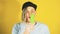 Young handsome satisfied man with dreadlocks in black cap eating ice cream on yellow background. Joyful guy in blue t