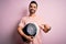 Young handsome slim sportsman with beard holding scale over isolated pink background very happy pointing with hand and finger