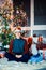 Young handsome smiles man in a cap sits by Christmas tree next to the window at night