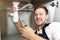 Young handsome smiling man plumber in uniform fixing the sink with pliers in his hand sitting on the kitchen floor