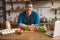 Young handsome smiling man sitting in well-equipped modern kitchen checking recipe for tasty breakfast in his laptop , weekend