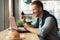 Young handsome smiling man works remotely in his laptop using his bank card for money tranfer in cafe eating croissant