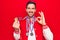 Young handsome sportsman winning medals standing over isolated red background doing ok sign with fingers, smiling friendly