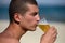 Young handsome sporty man drinking beer at the beach in summertime - relaxing, summer, thirsty concept. Resort relaxation. Sea in