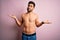 Young handsome strong man with beard shirtless standing over isolated pink background clueless and confused expression with arms