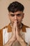 Young handsome stylish frowning man doing pray gesture folded hands