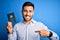 Young handsome tourist man holding australia australian passport id over blue background with surprise face pointing finger to