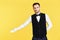 Young handsome waiter doing a welcome gesture over yellow background