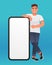 Young handsome white man points to the screen of a large smartphone. Advertising of a mobile application or services, promotion of