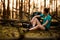 Young handsome woman in forest sits near fallen tree and looks away.