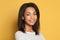 Young happy African American millennial woman with black hair smiling on yellow background, indoor portrait