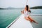 Young happy Asian woman enjoy and hold a wineglass sitting on deck of sailing yacht boat in bikini