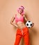 Young happy athletic woman with pink hair in bright sportswear standing and holding soccer ball in hand