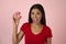 Young happy attractive Latin woman in red top smiling excited holding sugar donut on pink background