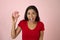 Young happy attractive Latin woman in red top smiling excited holding sugar donut on pink background