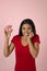 Young happy attractive Latin woman in red top smiling excited holding sugar donut on pink background