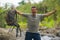 Young happy and attractive man with travel backpack hiking in river at forest feeling free enjoying nature and fresh environment