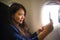 Young happy and beautiful Asian Chinese woman traveling for business inside airplane cabin smiling cheerful using mobile phone