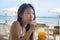 Young happy and beautiful Chinese Asian woman drinking healthy orange juice sitting at beach restaurant resort enjoying Summer hol