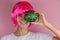 young happy beautiful woman with pink hair holding little watermelon near her face on a pink background