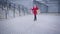 Young happy Caucasian woman in red coat and high black boots walking along the city square and leaving. Satisfied girl