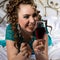 Young happy cheerful curly woman with glass of red wine and chocolate. Lady resting on the bed