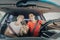 Young happy couple driving car and using smartphone while riding on road. Husband and wife looking at mobile phone together while